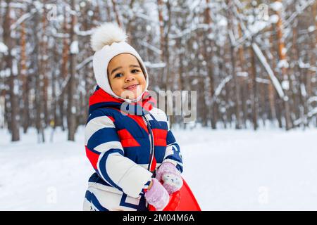 Ritratto invernale di felice bambina che indossa cappello a maglia e una tuta all'aperto in inverno Foto Stock