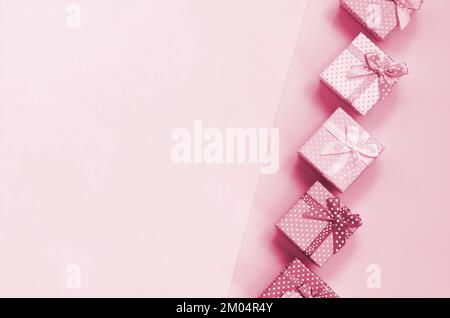 Piccole scatole regalo di diversi s con nastri si trova su uno sfondo. Immagine colorata in Viva Magenta, colore del 2023° anno Foto Stock