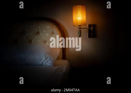 Un letto con una lampada illuminata appesa sopra il comodino Foto Stock