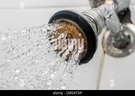 L'acqua scorre dal soffione della doccia collegato alle piastrelle del bagno. primo piano. Foto Stock