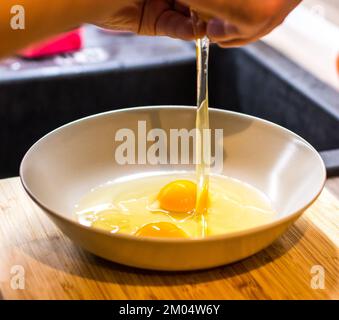 Spezzare con la mano l'uovo di pollo crudo nel recipiente. Foto Stock