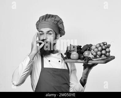 Cuocere con il viso soddisfatto in uniforme bordeaux contiene gli ingredienti per insalata Foto Stock