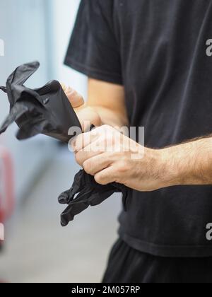 lo chef indossa guanti neri in una cucina professionale prima di cucinare filmati verticali Foto Stock