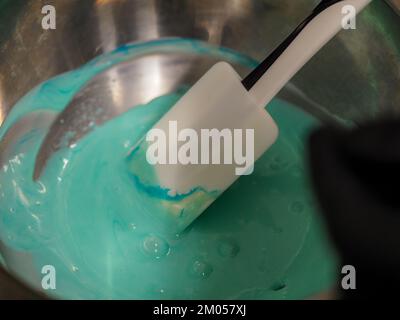 pasticciere mescolando il riempimento del sacchetto delle tubature mescolato con la vernice turchese commestibile per la graduazione del colore la guarnizione di torta smerigliata Foto Stock