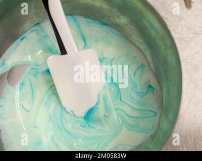 pasticciere mescolando il riempimento del sacchetto delle tubature mescolato con la vernice turchese commestibile per la graduazione del colore la guarnizione di torta smerigliata Foto Stock