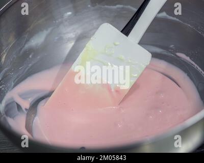 pasticciere mescolando il riempimento del sacchetto di tubatura mescolato con vernice rosa commestibile per la classificazione del colore e le riprese della guarnizione della torta Foto Stock