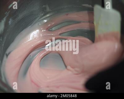 pasticciere mescolando il riempimento del sacchetto di tubatura mescolato con vernice rosa commestibile per la classificazione del colore e le riprese della guarnizione della torta Foto Stock