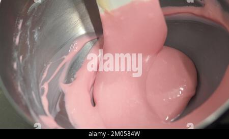 pasticciere mescolando il riempimento del sacchetto di tubatura mescolato con vernice rosa commestibile per la classificazione del colore e le riprese della guarnizione della torta Foto Stock