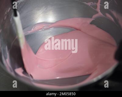 pasticciere mescolando il riempimento del sacchetto di tubatura mescolato con vernice rosa commestibile per la classificazione del colore e le riprese della guarnizione della torta Foto Stock