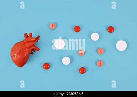 Modello di organo cardiaco accanto alle pillole su sfondo blu. Concetto per le malattie cardiache Foto Stock