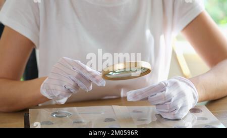 La numismatica femminile nei guanti esamina la sua collezione di monete a tavola. Foto Stock