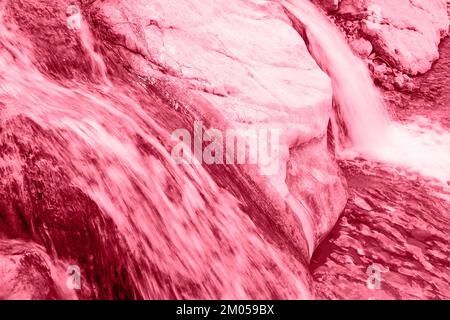 Chiudere una piccola cascata su un fiume di montagna in pietra. Esposizione lunga. Tonalità trendy nel colore 2023 Viva Magenta. Foto Stock