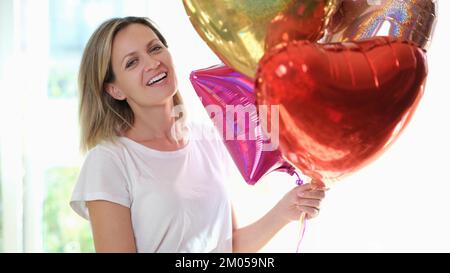 Felice donna bionda sorridente sta tenendo un sacco di palloncini colorati in mano. Foto Stock