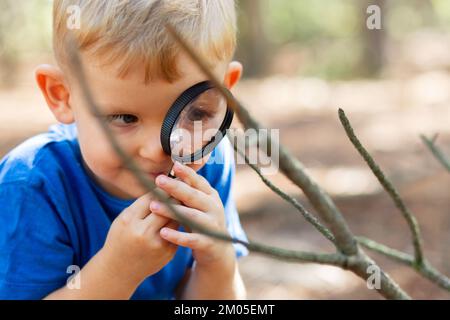 Il ragazzo curioso sta esplorando la natura con lente d'ingrandimento all'aperto Foto Stock
