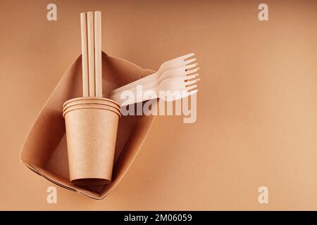 Stoviglie monouso ecocompatibili. Contenitori, tazze e forchette in carta Kraft su sfondo beige. Zero sprechi e concetto di plastica libera. Spazio di copia Foto Stock