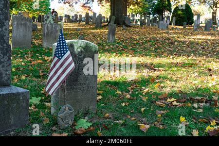 Primo piano della bandiera americana accanto alla storica lapide del soldato nel cimitero Sleepy Hollow. Stagione autunnale nel cimitero. Foto Stock