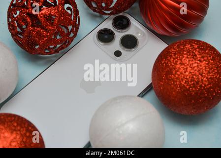 Riga/Lettonia - 4 dicembre 2022: Nuovo telefono moderno iPhone 14 pro tra le scintillanti decorazioni natalizie su sfondo nero. Regalo di Natale conce Foto Stock