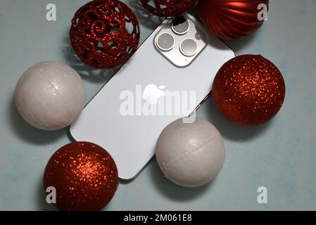 Riga/Lettonia - 4 dicembre 2022: Nuovo telefono moderno iPhone 14 pro tra le scintillanti decorazioni natalizie su sfondo nero. Regalo di Natale conce Foto Stock