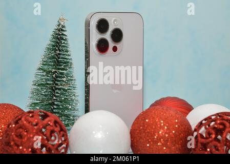Riga/Lettonia - 4 dicembre 2022: Nuovo telefono moderno iPhone 14 pro tra le scintillanti decorazioni natalizie su sfondo nero. Regalo di Natale conce Foto Stock