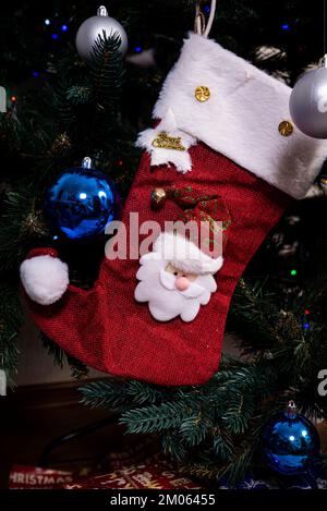 Calza di Natale. Calza rossa con fiocchi di neve per i regali di Babbo Natale appesi sull'albero di Natale. Decorazioni per le vacanze invernali Foto Stock