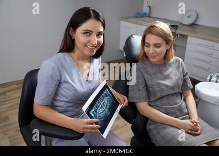 Dentista femminile che indica l'immagine radiologica del paziente in studio dentistico Foto Stock