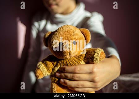 Ragazza che mostra la fotocamera il suo orsetto marrone in una stanza rosa con illuminazione a contrasto Foto Stock