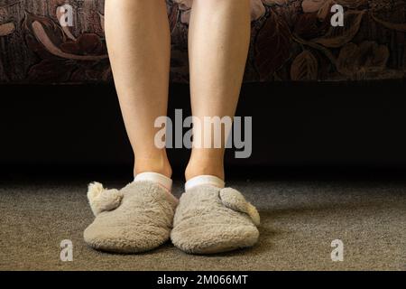 piedi femminili in pantofole grigie sul tappeto nella camera da letto, piedi in pantofole, comfort di casa Foto Stock
