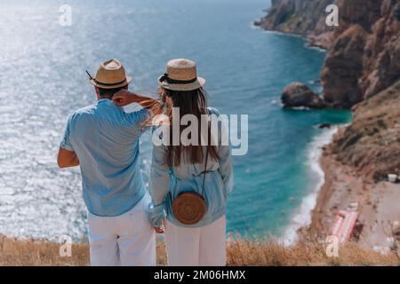 La coppia si alza con le spalle al pubblico e guarda verso il basso il bel mare. Indossano cappelli, camicie blu e pantaloncini bianchi. Foto Stock