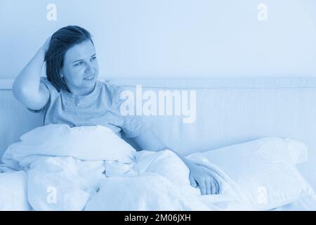 Donna sorridente bruna con pajama seduta a letto in camera da letto Foto Stock