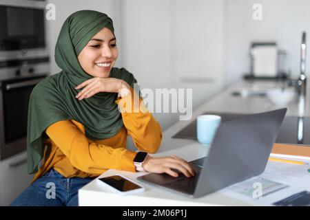 Commercio in linea. Giovane donna musulmana in Hijab che lavora con il laptop a casa Foto Stock