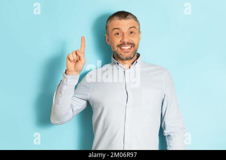 Eureka, concetto di gesti. Uomo caucasico maturo eccitato che punta il dito indice verso l'alto e sorridente sullo sfondo blu dello studio Foto Stock