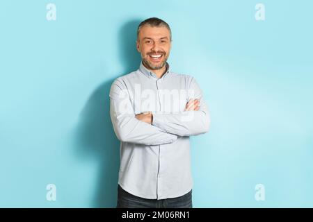 Ritratto maschile. Felice uomo caucasico di mezza età con braccia piegate sorridendo alla macchina fotografica, posando su sfondo blu studio Foto Stock