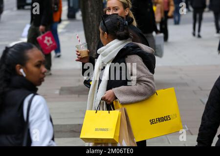 Uno shopping natalizio con le borse per lo shopping Selfridges a Oxford Street nel West End di Londra. Gli acquirenti approfittano delle offerte e, secondo una recente ricerca di Deloitte, il 54% degli acquirenti probabilmente acquisterà per Natale nelle prime due settimane di dicembre. Foto Stock