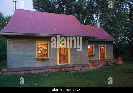 Vecchio circa 1840 Canadiana stile cottage verde dipinto con rifiniture gialle e rosso lamiera tetto log casa al crepuscolo. Foto Stock