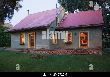 Vecchio circa 1840 Canadiana stile cottage verde dipinto con rifiniture gialle e rosso lamiera tetto log casa al crepuscolo. Foto Stock