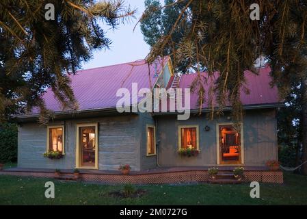 Vecchio circa 1840 Canadiana stile cottage verde dipinto con rifiniture gialle e rosso lamiera tetto log casa al crepuscolo. Foto Stock