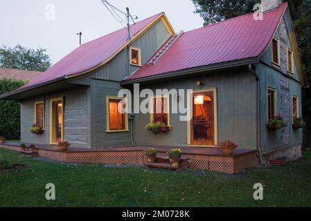 Vecchio circa 1840 Canadiana stile cottage verde dipinto con rifiniture gialle e rosso lamiera tetto log casa al crepuscolo. Foto Stock