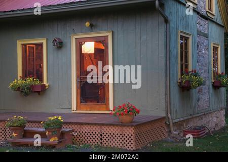 Vecchio circa 1840 Canadiana stile cottage verde dipinto con rifiniture gialle e rosso lamiera tetto log casa al crepuscolo. Foto Stock