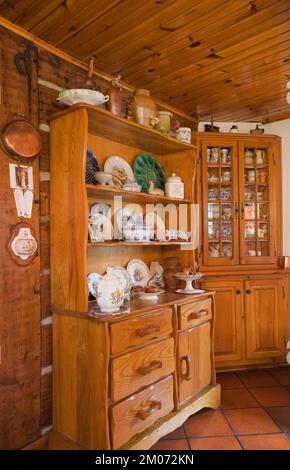 Buffet di antiquariato con collezione assortita di chinaware e curiosità in cucina all'interno di una casa di legno in stile cottage ricostruita degli anni '1800. Foto Stock