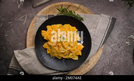 FARFALLE pasta con salsa di zucca in un piatto di ceramica su un piano cucina in pietra scura. Foto Stock