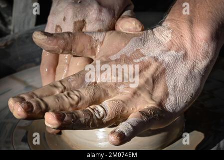 Un primo piano di due mani bagnate che formano un cono di argilla in una ciotola su una ruota di ceramica in una dimostrazione alla fiera d'arte di Tucson, Arizona Foto Stock