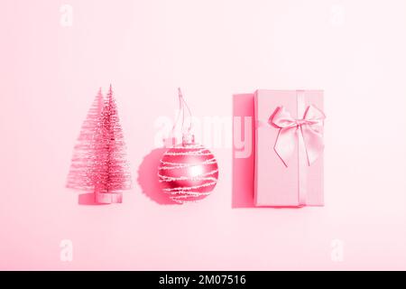 Confezione regalo, palla di Natale e abete giocattolo su sfondo rosa con ombre affilate. Composizione minima. Vista dall'alto, disposizione piatta. Foto Stock