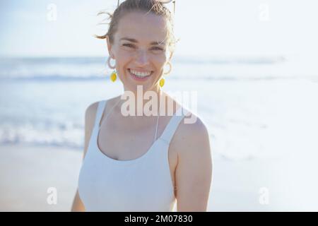 Ritratto di felice donna moderna in costume da bagno bianco in spiaggia. Foto Stock