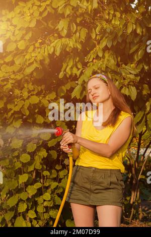 Bella giovane donna sorridente innaffiare le piante nel suo giardino con un tubo da giardino. concetto di hobby Foto Stock