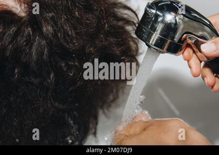 Splendida donna anziana allegra gode di un massaggio alla testa mentre lava i capelli da un parrucchiere professionista. Bellezza, acconciatura, moda, stile di vita Foto Stock