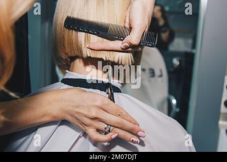 Il primo piano di un parrucchiere taglia i capelli bianchi bagnati di un cliente in un salone. Il parrucchiere taglia una donna. Vista laterale di una mano che taglia i capelli con le forbici Foto Stock