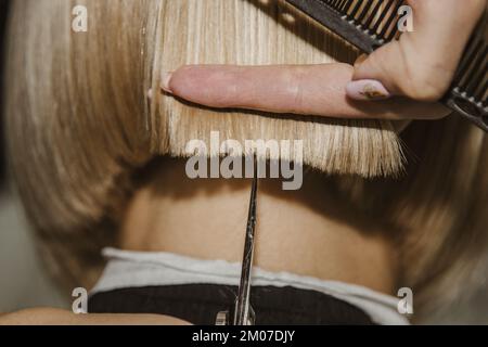 Il primo piano di un parrucchiere taglia i capelli bianchi bagnati di un cliente in un salone. Il parrucchiere taglia una donna. Vista laterale di una mano che taglia i capelli con le forbici Foto Stock