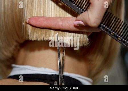 Il primo piano di un parrucchiere taglia i capelli bianchi bagnati di un cliente in un salone. Il parrucchiere taglia una donna. Vista laterale di una mano che taglia i capelli con le forbici Foto Stock