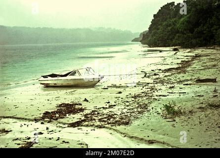 Una barca è parcheggiata sulla spiaggia sabbiosa quando piove sull'isola di Peucang nel Parco Nazionale di Ujung Kulon, Pandeglang, Banten, Indonesia. Foto Stock