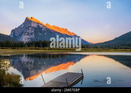 Un molo in legno si estende nel Two Jack Lake nel Banff National Park, con il monte Rundle che si innalza drammaticamente alle sue spalle nelle Montagne Rocciose canadesi. Foto Stock